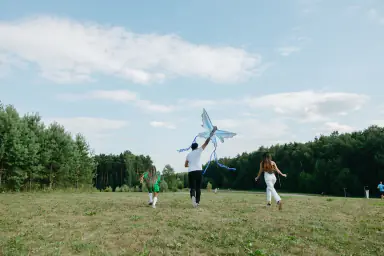 Family running away from the camera while lifting a kite in a park