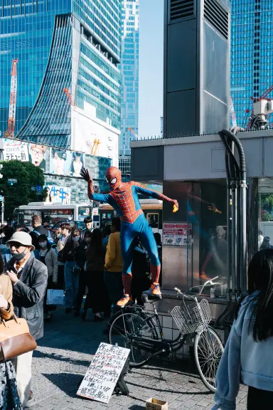 Spider-Man cosplayer balancing on a bicycle above a Shibuya street crowd